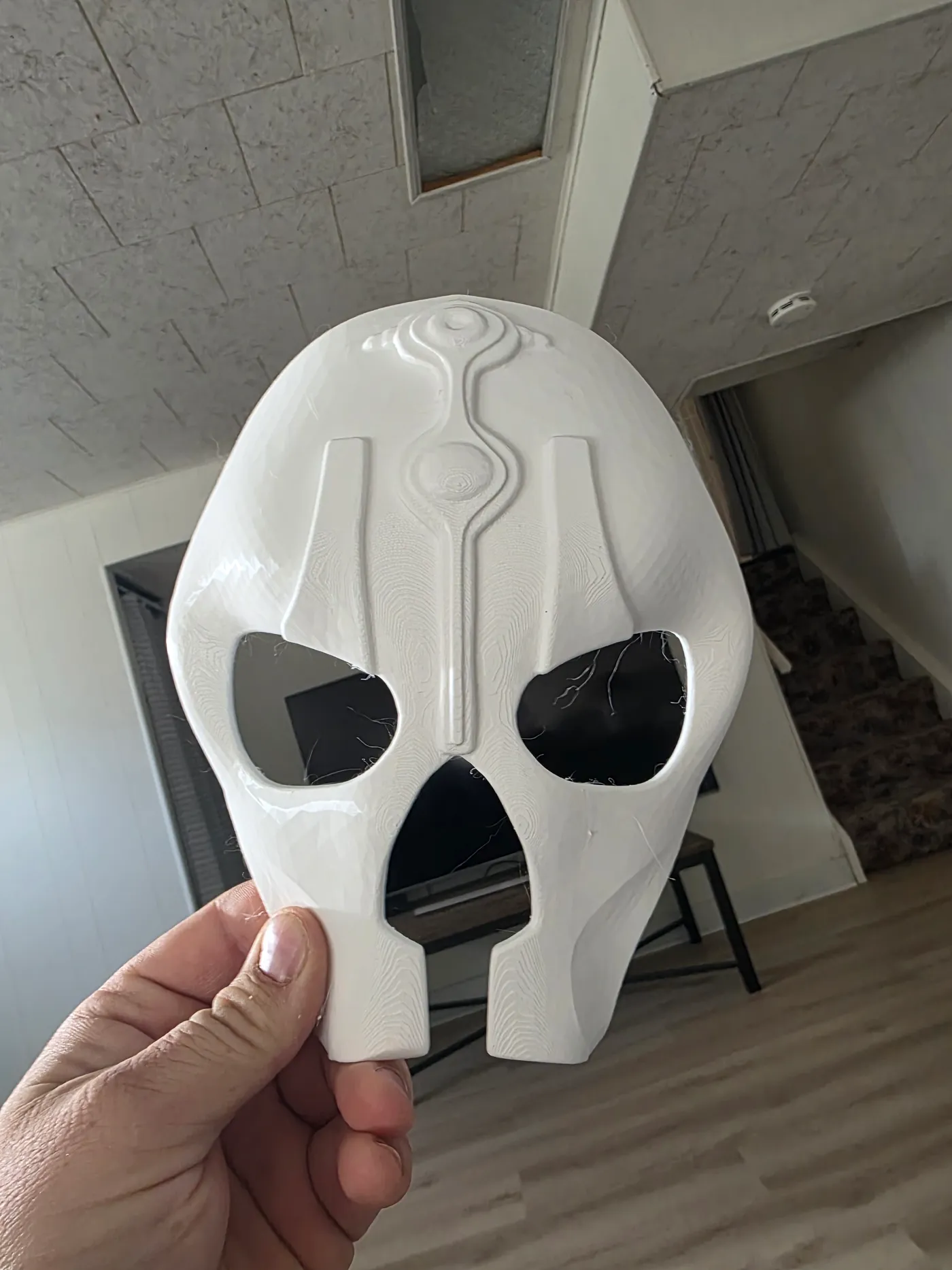 Hand holding a white PETG mask print showing layer lines and fine stringing in the eye openings