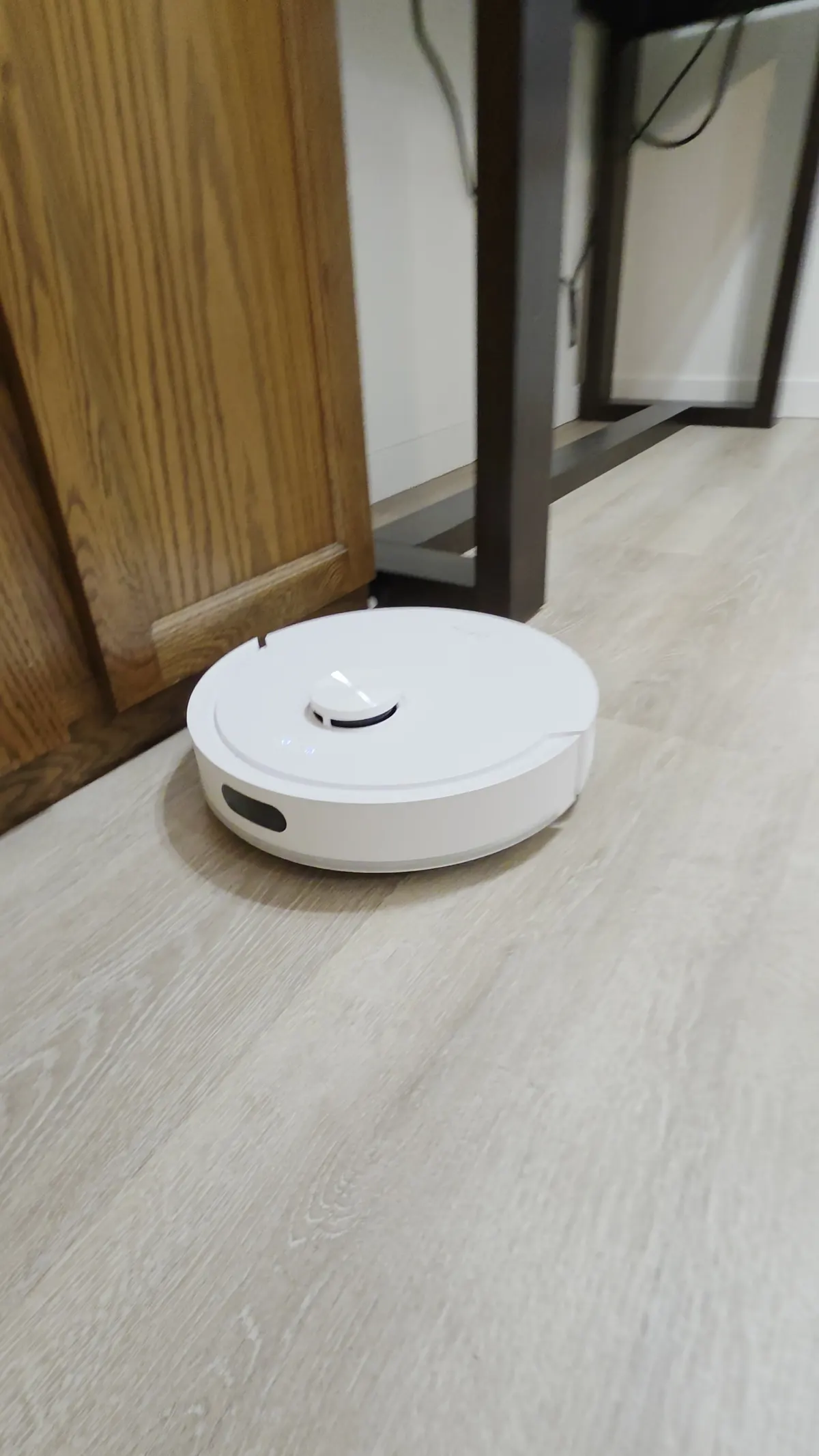Dreame D20 Air Plus cleaning beside wooden cabinet doors and a desk leg