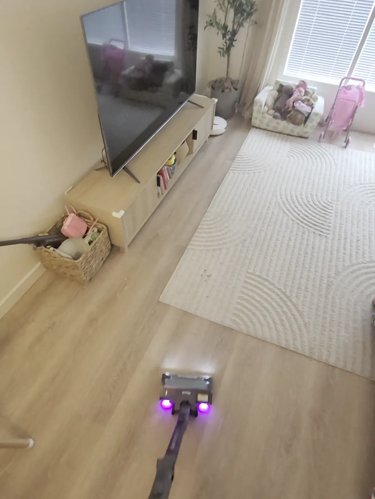First-person view of the Shark PowerDetect with lit floor head crossing vinyl plank floor toward a cream area rug