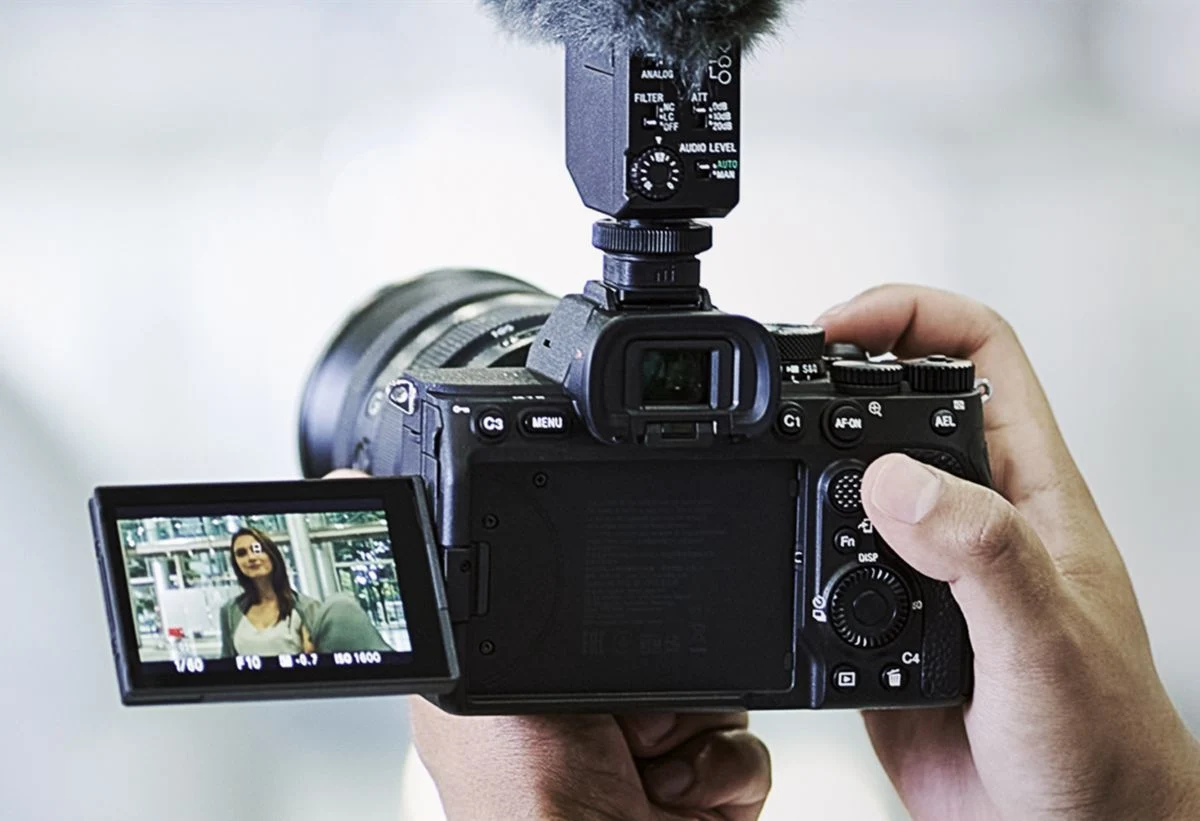Sony shows the Alpha 7 IV used for handheld filming with an optional lens.