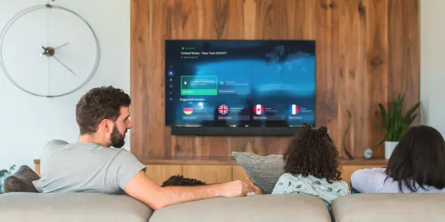 A family on a couch watching a TV that shows the NordVPN app connected to a server